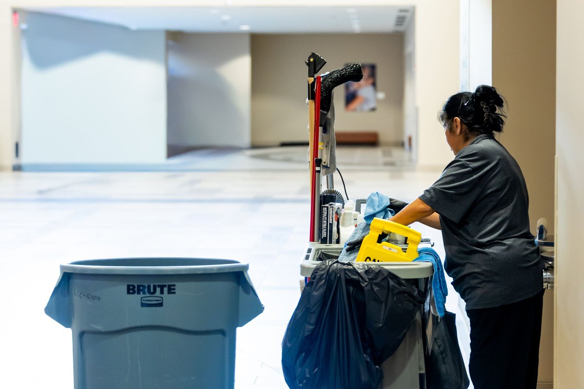 Janitorial staff member with a cleaning cart in a bright building hallway
