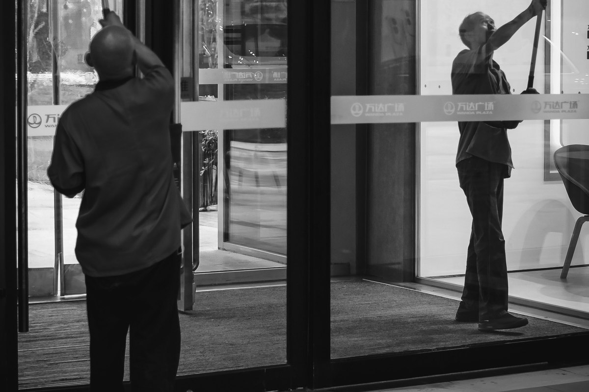 Two janitors cleaning the glass entrance doors of a commercial office building