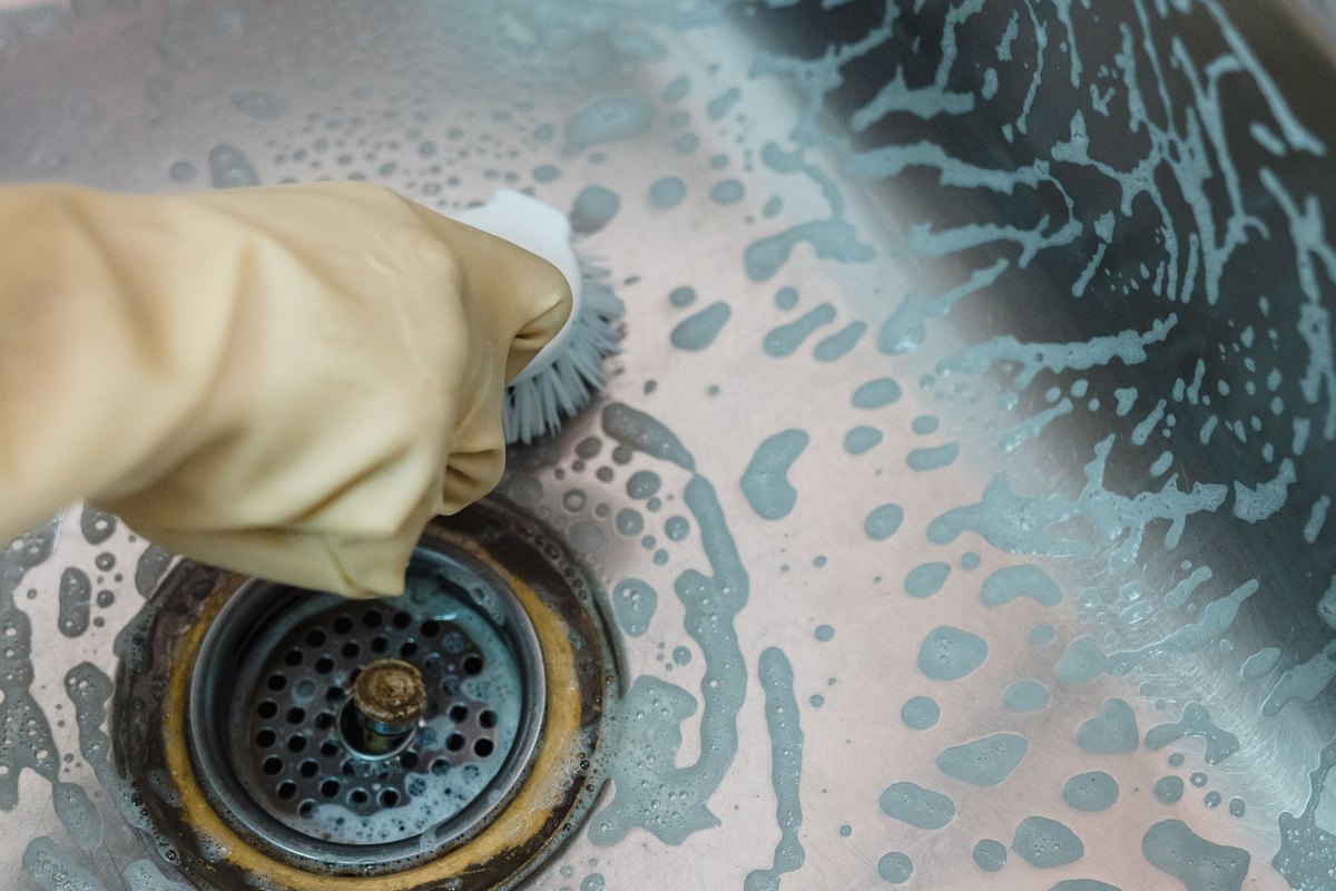 Gloved hand scrubbing a stainless steel sink during a deep clean